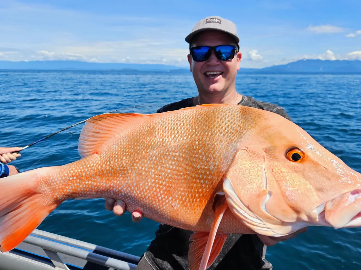 Person holding a large orange fish on a boat with the ocean in the background.