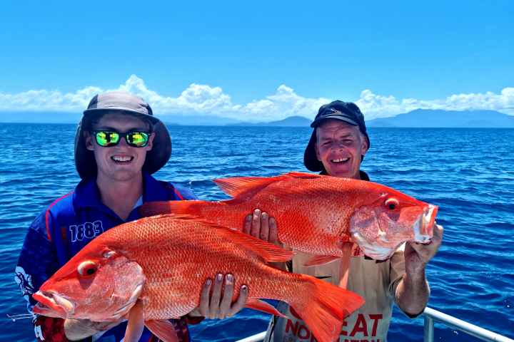 two people with re fishes on boat in water