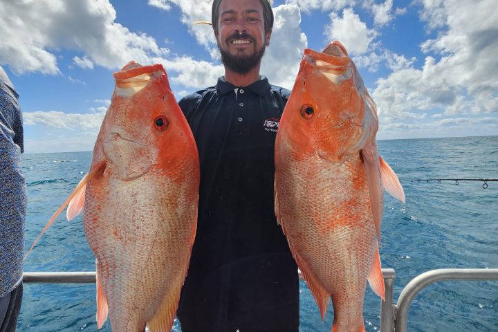 Person on a boat holding two large orange fish with a bright sky in the background.