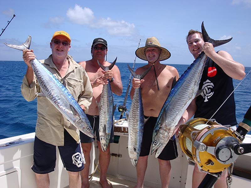 Four men on a boat holding large fish with ocean background.