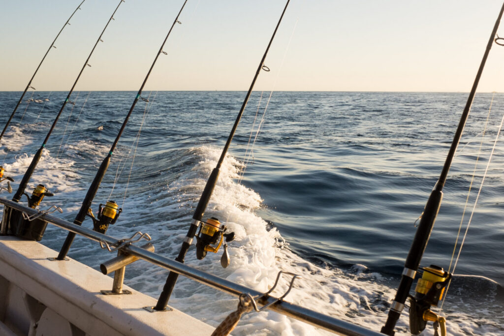 Fishing rods on a boat with ocean waves in the background at sunset.