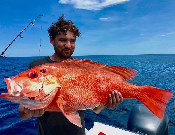 Person holding large red fish on a boat under a blue sky.
